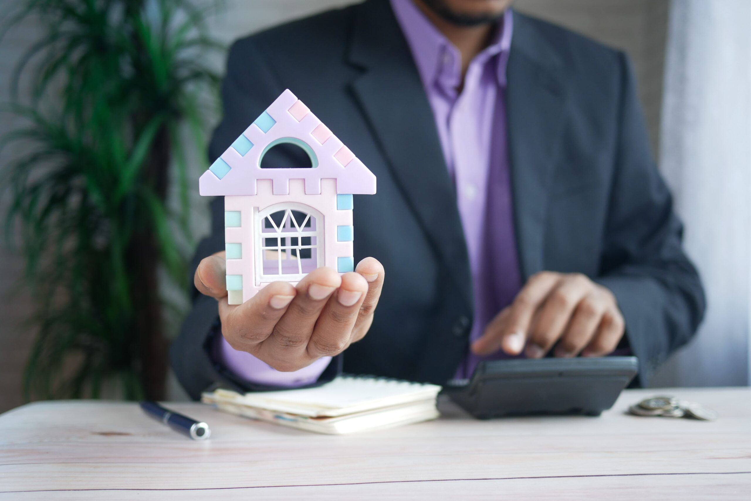 Why South Florida Property Owners Are Switching to Full-Service Management in 2026 (And What It Means for Your Portfolio) Businessman in suit holds model house, calculates real estate investments.